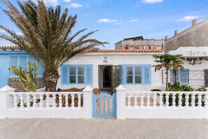 A white building with blue shutters, a gate, and a palm tree. - Home2Book Oceanfront Bliss in Taliarte (Taliarte)