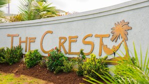 A sign with the text "THE CREST" and a palm tree symbol, surrounded by greenery. - Sunshine Paradise Villa (St. Ann's Bay)