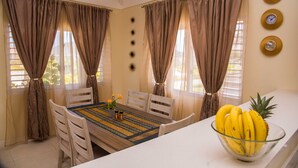 A dining area with a table set for four, curtains, a clock, and a bowl of bananas. - Sunshine Paradise Villa (St. Ann's Bay)