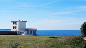 Ein modernes weißes Haus mit großer Garage, gelegen auf einem grasbewachsenen Hügel mit Blick auf ein ruhiges Meer.