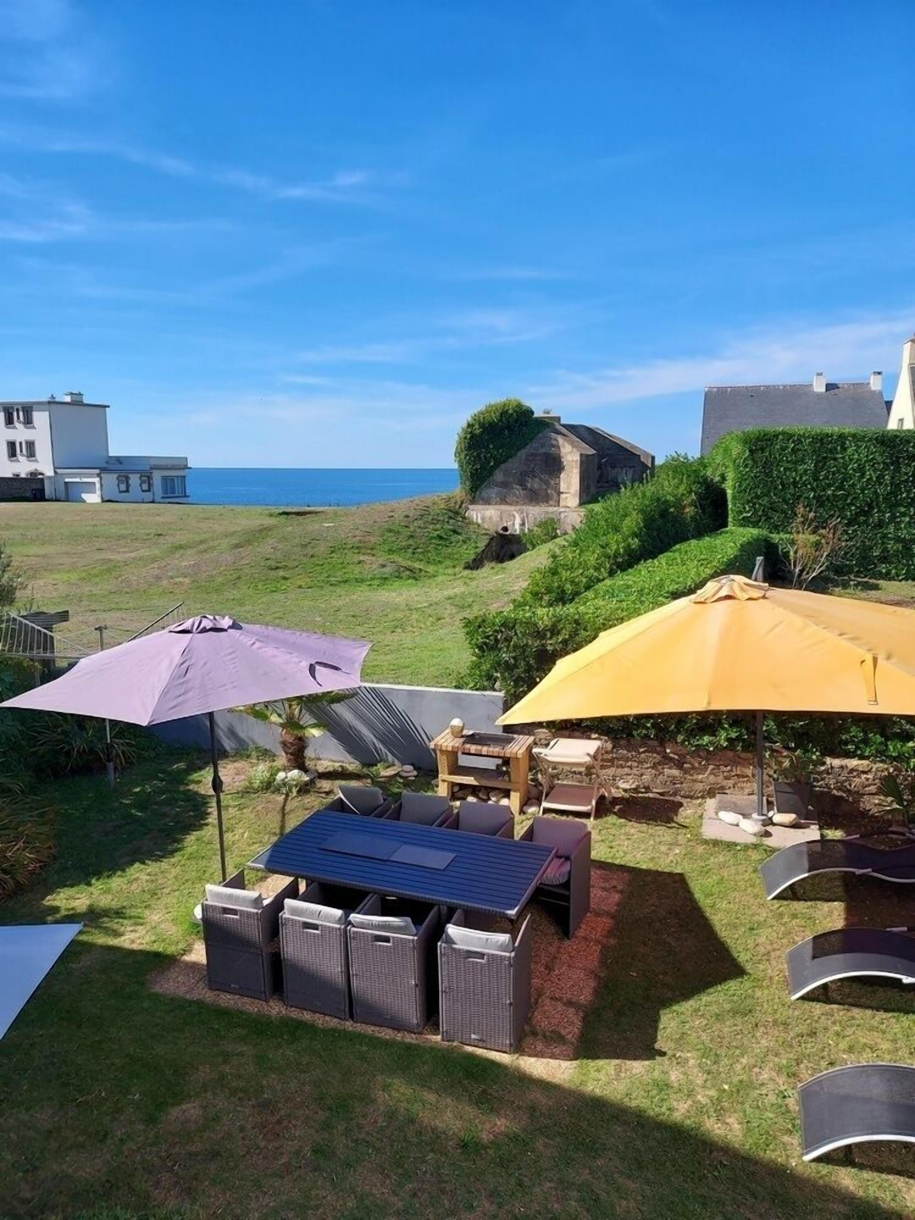A patio area with outdoor furniture, umbrellas, and a view of the sea.