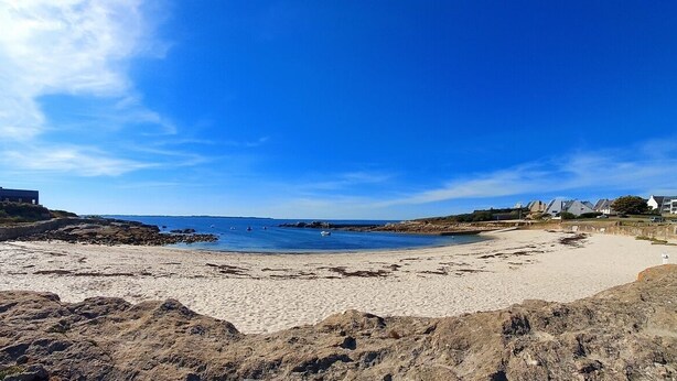 Ein Strand mit felsigem Vordergrund, einem Sandstrand und Gebäuden im Hintergrund.