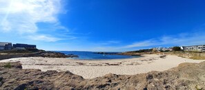 A beach with rocky foreground, a sandy shore, and buildings in the background. - Ty Relax - Ploemeur - Gîte (PLOEMEUR)