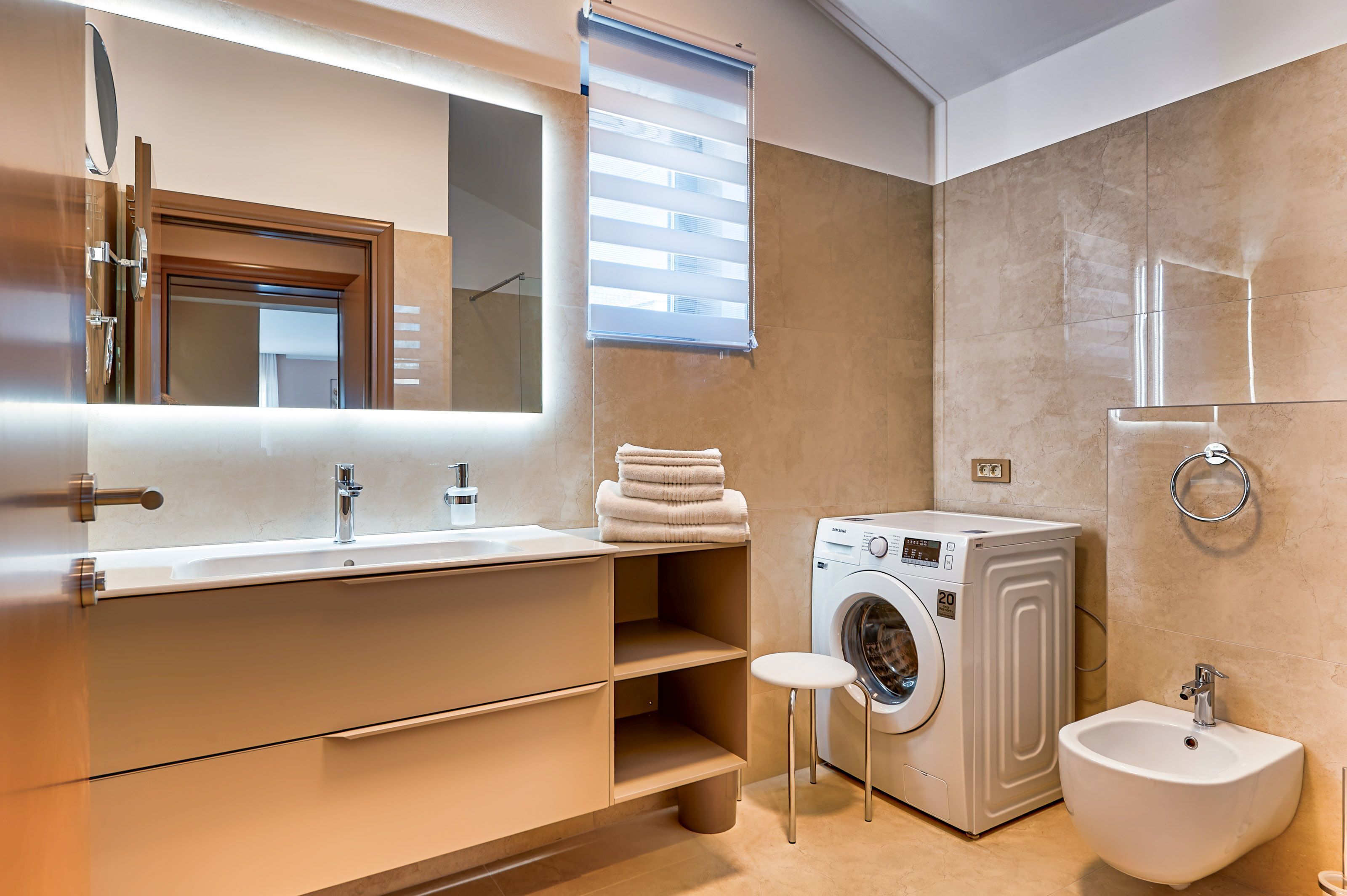 A modern bathroom with a large mirror, a sink, a washing machine, and a bidet.