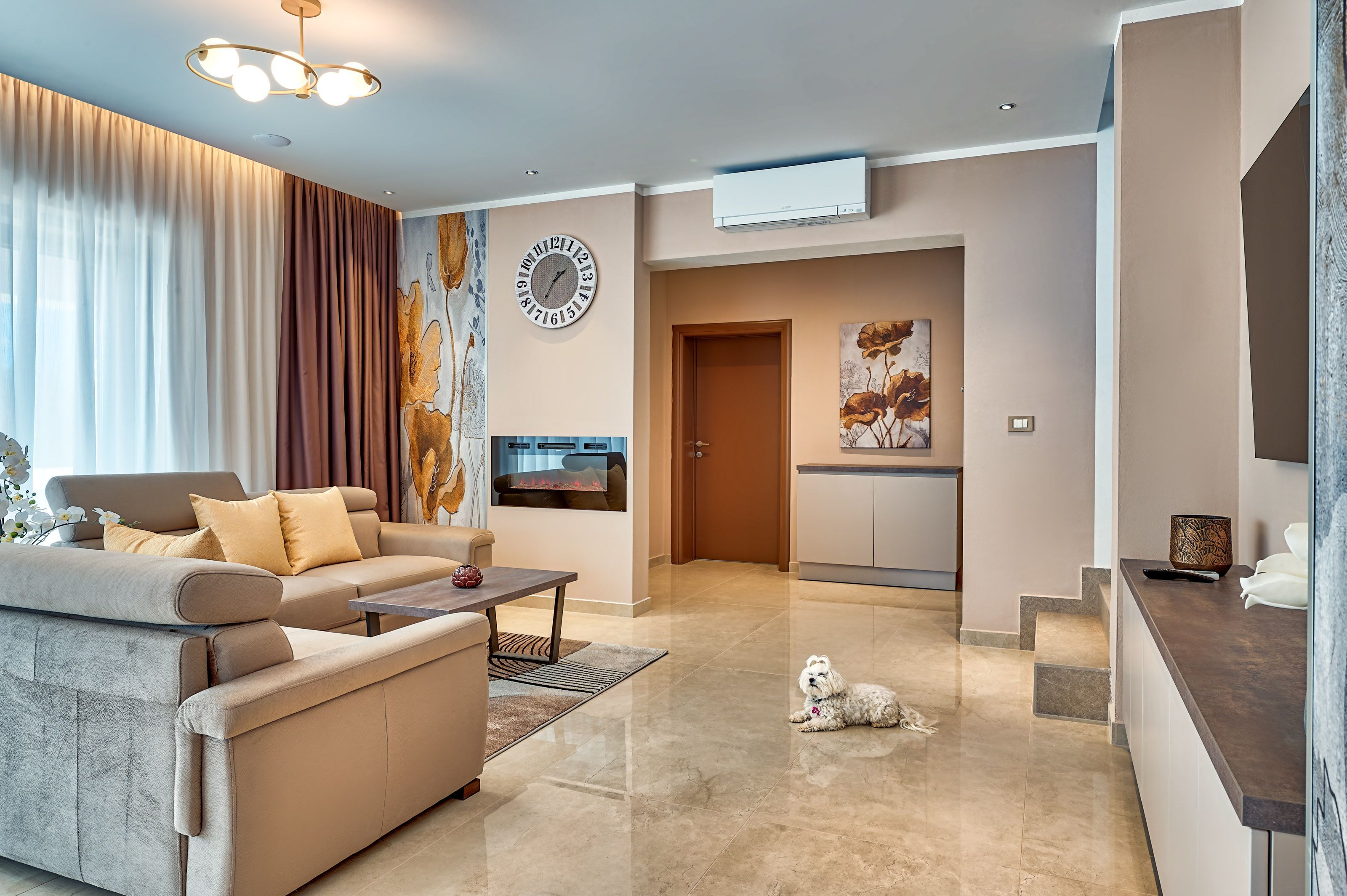 A modern living room with a sofa, coffee table, and a dog. There is a kitchen area with a microwave and a painting on the wall.