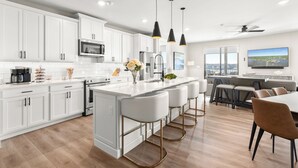 A modern kitchen with white cabinets, a central island with bar stools, a built-in oven, and a large window overlooking a cityscape. - NEW Luxury Lakefront Condo w/ 2 Master Suites! 4D (Lake Ozark)