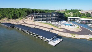 A modern hotel with multiple floors, a dock area with boats, and a river view. - NEW Luxury Lakefront Condo w/ 2 Master Suites! 4D (Lake Ozark)