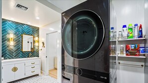 Une salle de bain moderne avec un grand lave-linge noir, un meuble-lavabo blanc doté de poignées dorées et un pare-feu en motif chevrons.
