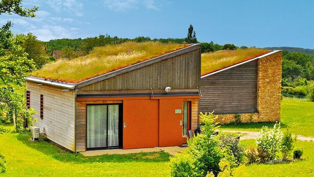 A modern building with a sloped roof, a large glass door, and a small attached structure.