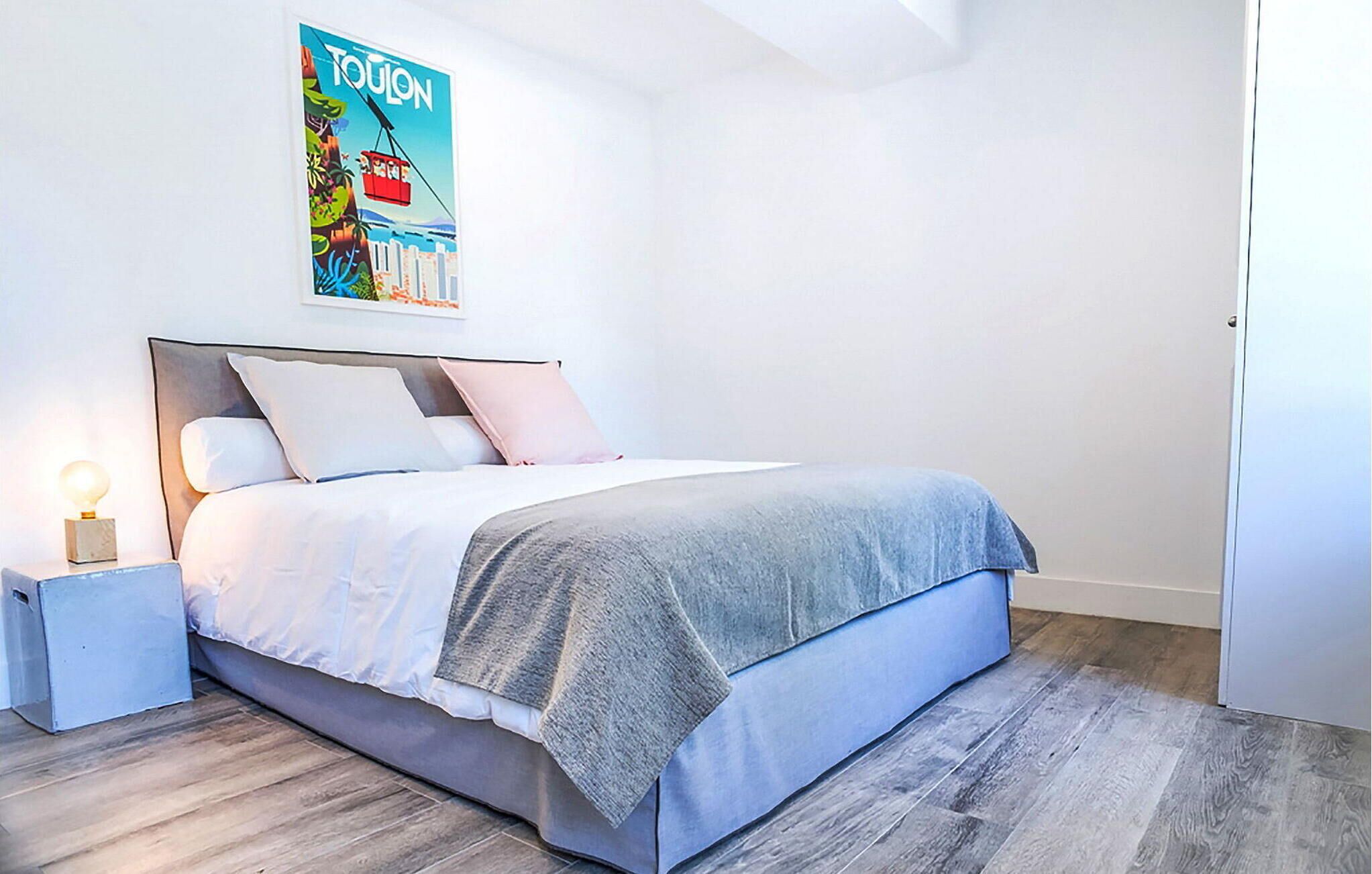 A modern bedroom with a bed, a nightstand, a poster on the wall, and a wooden floor.