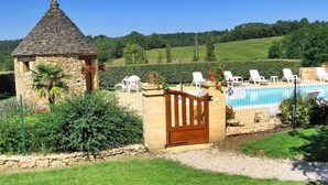 A stone building with a conical roof, a pool with lounge chairs, and a gate. - La Grange Des Endrevies (Sarlat La Caneda)