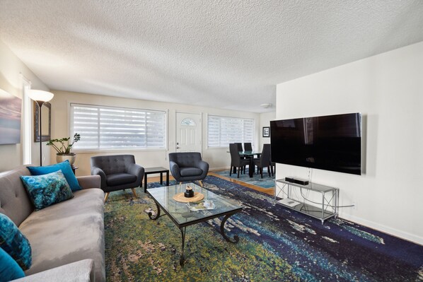 Una sala de estar con un sofá, dos sillones, una mesa de centro, un televisor y un comedor con sillas y una mesa.