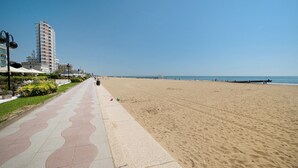A beach with a paved walkway, a tall building, and a pier in the distance. - Apartment 'Condominio Lara A16' with Private Terrace and Air Conditioning (Jesolo)