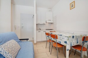 A compact living space with a kitchenette, a dining table with chairs, and a sofa with a patterned cushion.