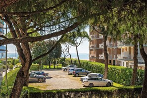 A parking area with cars, trees, and a building with balconies.