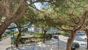 A tree-lined street with parked cars and a building in the background. - Apartment 'Condominio Lara A16' with Private Terrace and Air Conditioning (Jesolo)
