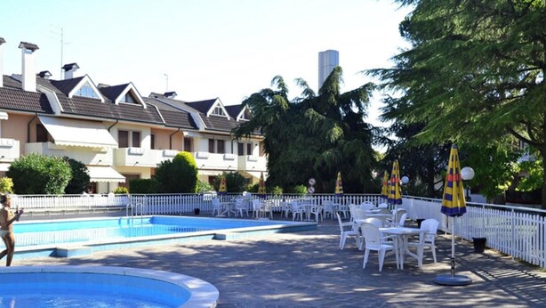 Una piscina amb gandules i ombrel·les, envoltada per una tanca blanca i arbres.