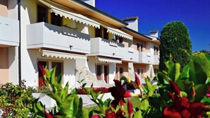 Un hotel de diversos pisos amb balcons, un jardí ben cuidat i un cel blau i clar.