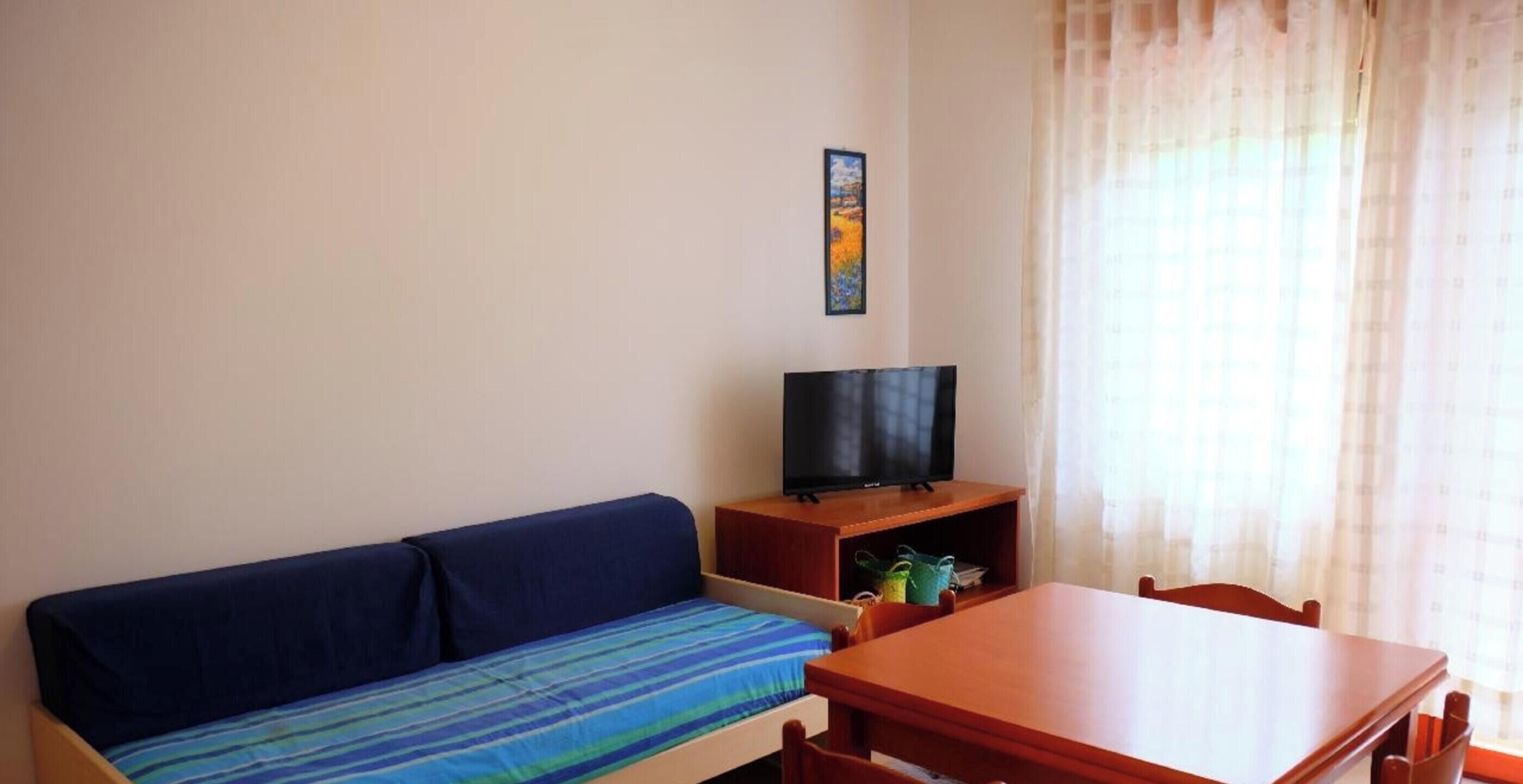 Ein Zimmer mit einer Couch, einem Fernseher auf einem Holzboden, einem Tisch und Stühlen.