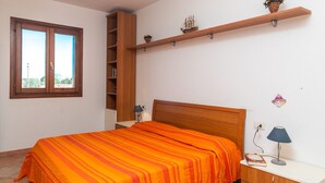 Une chambre à coucher comprenant un lit, une table de chevet, une lampe, une étagère avec des objets décoratifs et une fenêtre.