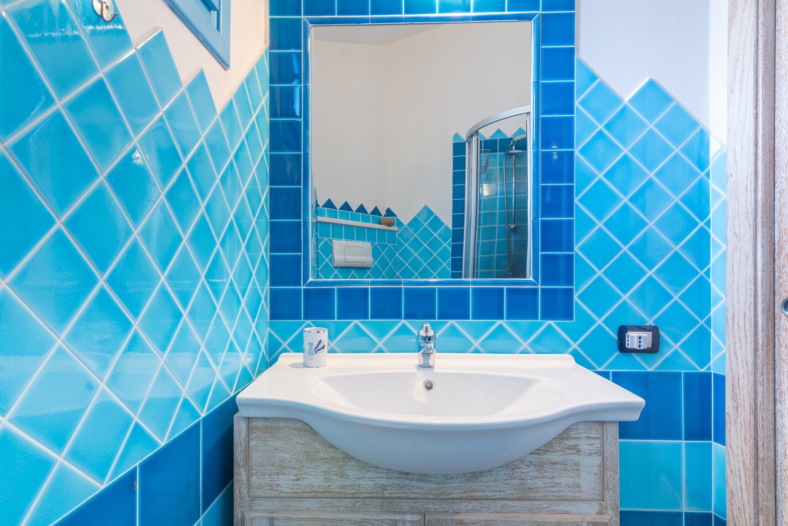 Un baño con un lavamanos blanco, un espejo y paredes con azulejos azules.