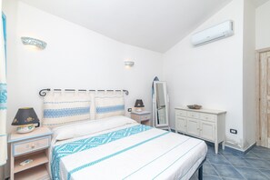 Une chambre à coucher comprenant un lit, une table de chevet, une lampe, une commode, un miroir et un appareil de climatisation.
