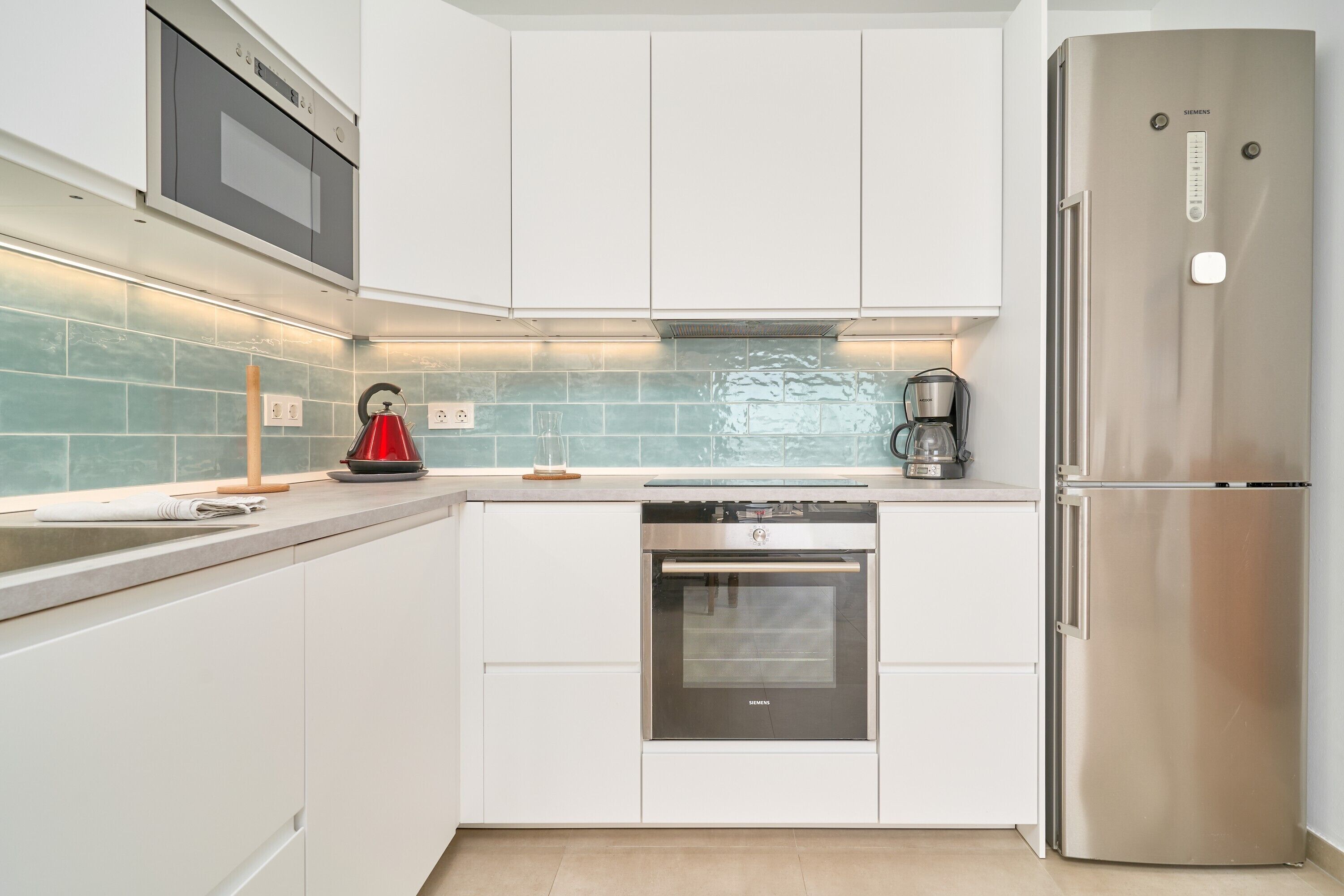 Una cocina moderna con armarios blancos, horno de acero inoxidable, refrigerador y salpicadero de azulejos.