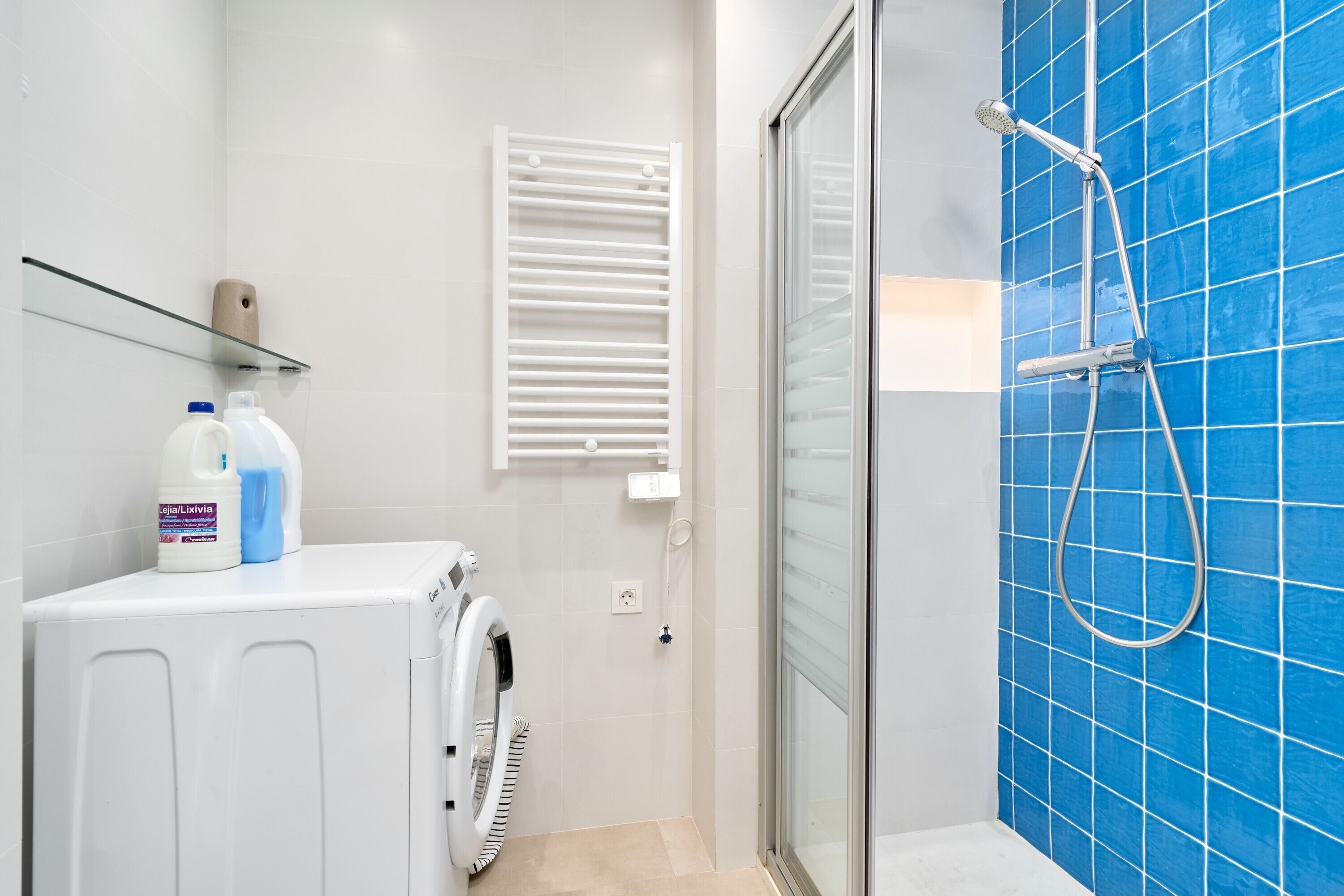 Une salle de bain avec une douche à parois de verre, un lave-linge et une étagère contenant des produits de nettoyage.