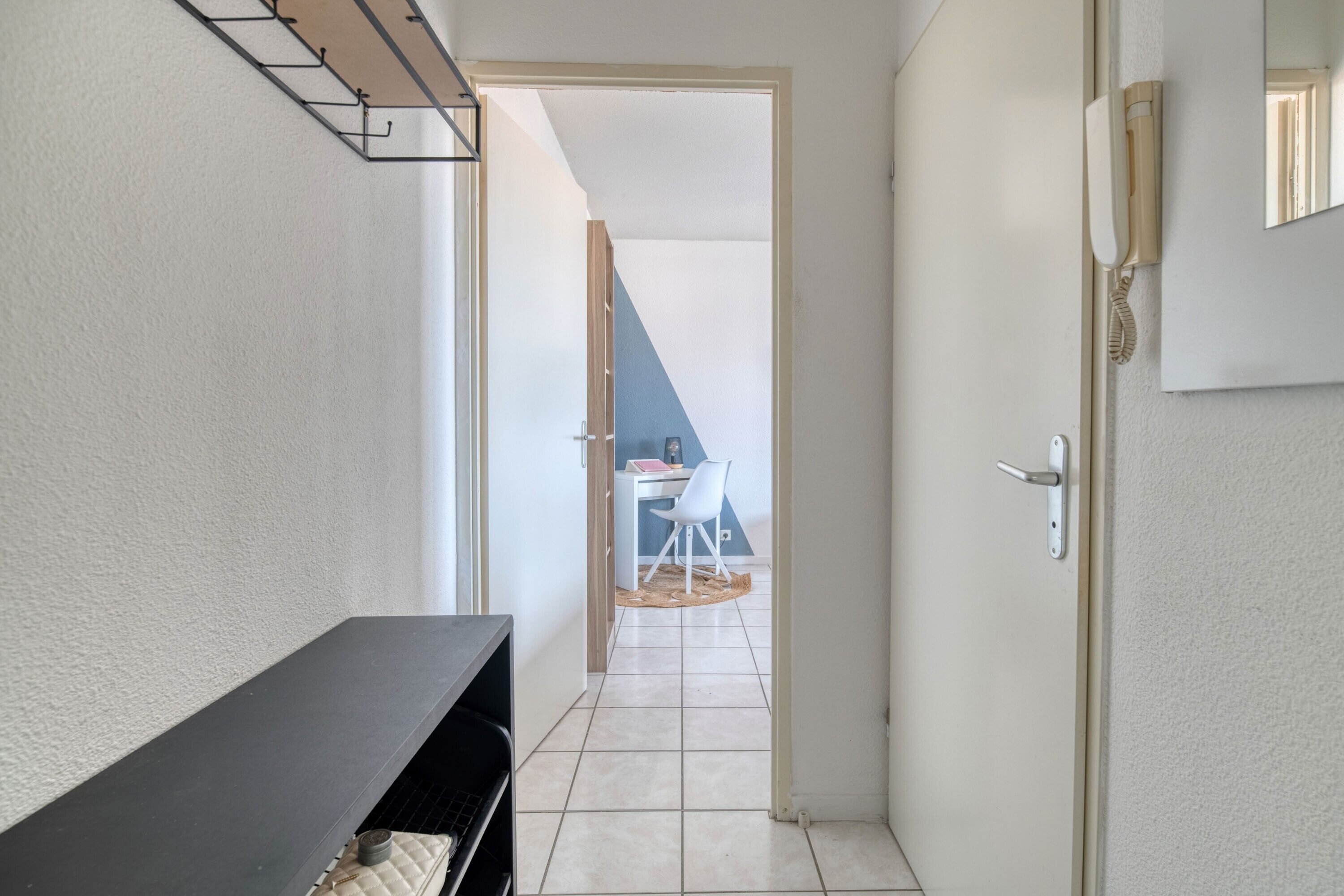 A hallway with a black console table, a white door, and a view into a room with a desk and chair.