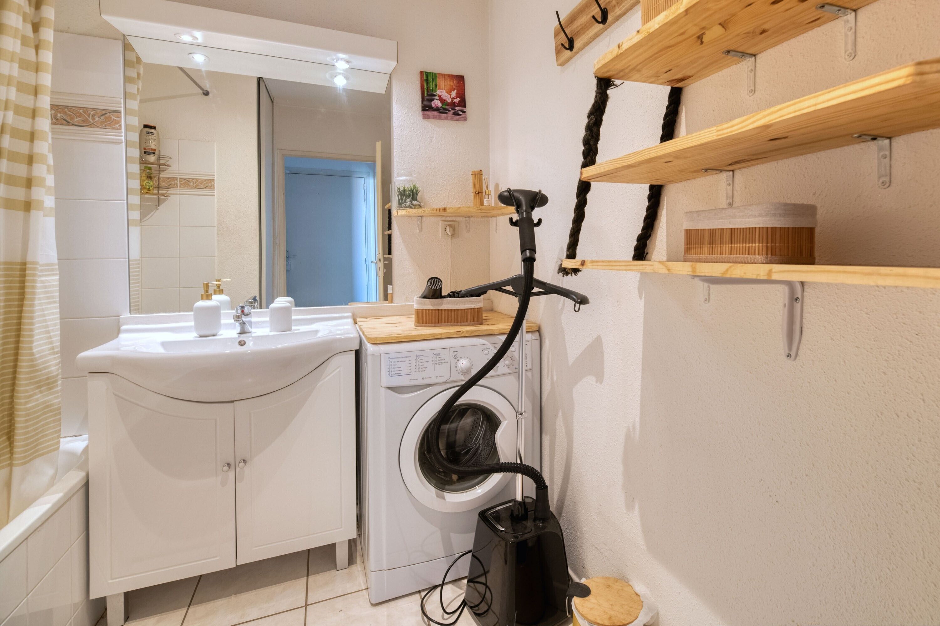 A compact bathroom with a sink, mirror, and a washing machine.
