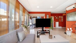 A modern living room with a sofa, coffee table, TV, and a large window. - Holiday Home 'Goleta' with Private Pool, Wi-Fi and Air Conditioning (El Puerto de Santa María)