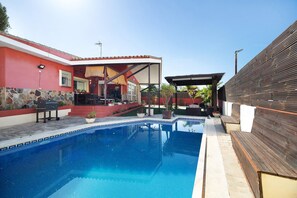A swimming pool with a stone border, a covered patio, and a wooden deck.