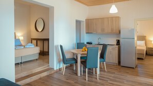 Habitación de hotel compacta con cama, una pequeña zona de comedor con mesa y sillas, cocina con armarios y un refrigerador, y techo de madera.