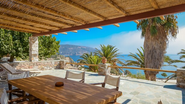 Una mesa de madera con sillas, un muro de piedra y vistas al mar.