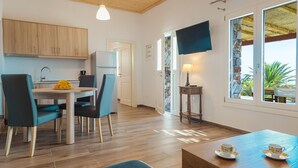 Una cocina moderna con armarios de madera, una mesa de comedor con sillas, un televisor montado en la pared y una ventana con vista a la vegetación.