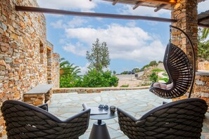 Une terrasse en pierre avec des chaises et une table en osier, offrant une vue sur une plage et une végétation luxuriante.