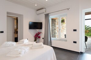 Un dormitorio con cama, toallas, televisor, pared de piedra y puerta que da a un espacio exterior.