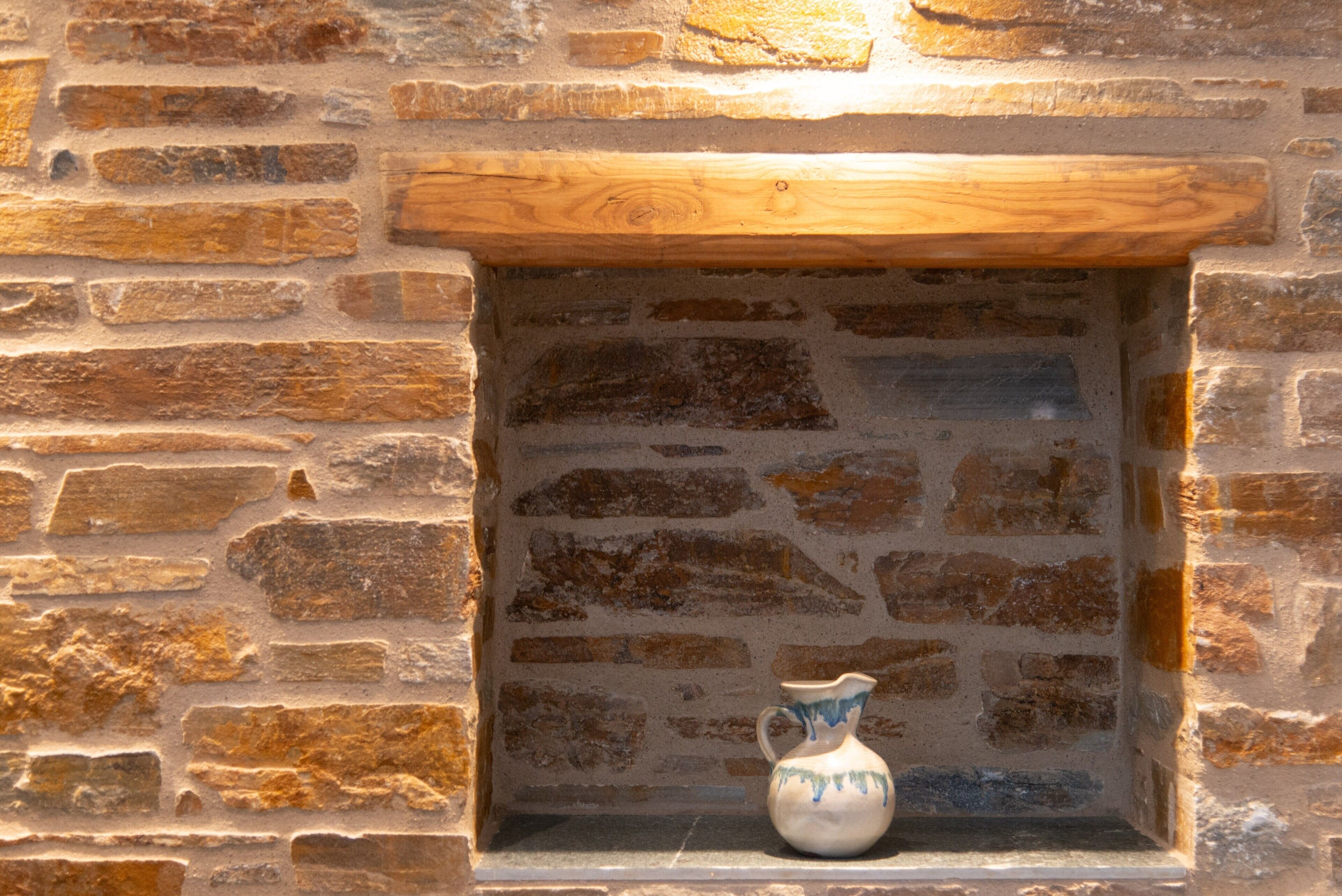 A stone wall with a wooden shelf and a ceramic pitcher.
