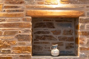 Un muro de piedra con un estante de madera y una jarra de cerámica.