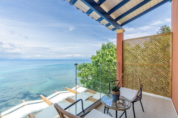 A balcony with a view of the ocean, a table with chairs, and a potted plant.