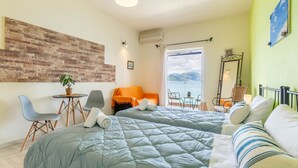 A hotel room with two beds, a small table with chairs, a potted plant, and a view of the sea. - Studio Apartment 'Nikos Seaside  5' with Sea View, Wi-Fi and Air Conditioning (??????a)