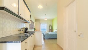 A kitchen with a countertop, sink, and cabinets, a bedroom with a bed and window, and a hallway leading to a door. - Studio Apartment 'Nikos Seaside  5' with Sea View, Wi-Fi and Air Conditioning (??????a)