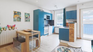 A modern kitchen with blue cabinets, a dining area with a wooden table, and a view of the outside. - Villa 'Oasis Tropicale A Cleguerec' with Private Terrace, Private Garden and Wi-Fi (CLEGUEREC)