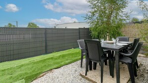 An outdoor patio with a table and chairs, a small lawn, and a fence. - Villa 'Oasis Tropicale A Cleguerec' with Private Terrace, Private Garden and Wi-Fi (CLEGUEREC)