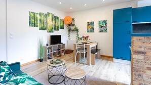 A living room with a sofa, a TV, a dining table with chairs, a bookshelf, and a blue cabinet. - Villa 'Oasis Tropicale A Cleguerec' with Private Terrace, Private Garden and Wi-Fi (CLEGUEREC)