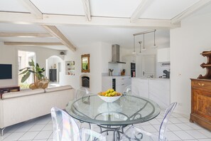 A modern kitchen with white cabinets, a dining area with a glass table, and a sofa. - Villa "Chez Dominique" with Private Pool, Private Terrace and Wi-Fi (Manosque)