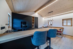Une cuisine moderne avec un plafond en bois, un long comptoir et deux tabourets de bar bleus.