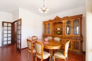 A dining area with a wooden table and chairs, a cabinet with glass doors, and a chandelier.
