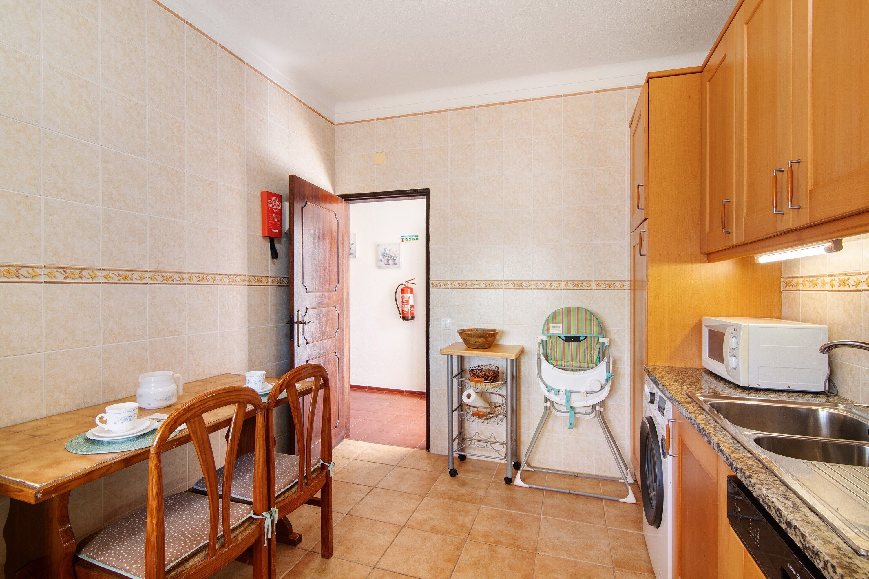 A kitchen with a dining table, chairs, a washing machine, a microwave, and a sink.