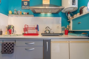 A kitchen with a modern design, featuring a stainless steel range hood, a kettle, and various kitchen utensils on the counter.